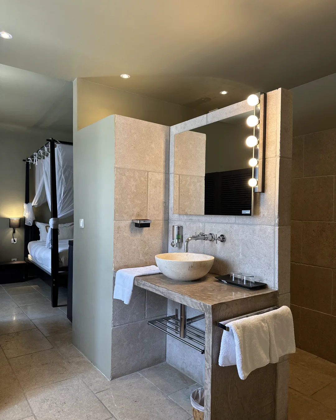 Salle de bains ouverte sur la chambre, vasque en pierre et miroir à ampoules, chambre Bali, Lourmarin