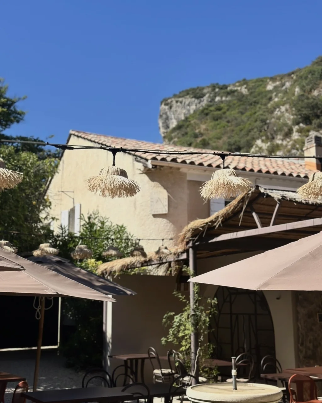 Façade provençale et parasols de la terrasse au pied de la falaise du Luberon, hôtel O Mamma Mia à Lourmarin