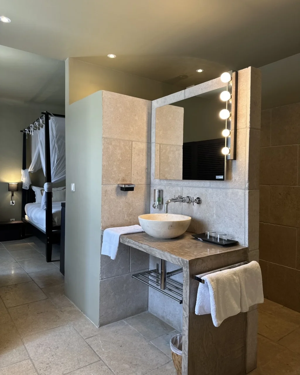 Vasque en pierre et miroir bordé d'ampoules ouvrant sur le lit à baldaquin, hôtel O Mamma Mia à Lourmarin