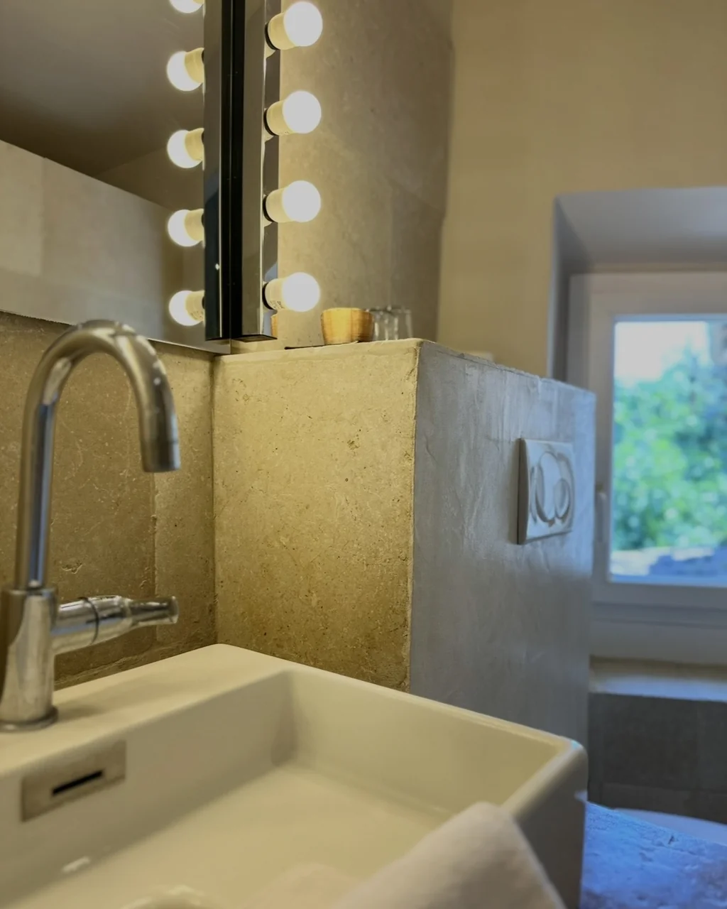 Salle de bains en pierre, vasque et miroir bordé d'ampoules, hôtel O Mamma Mia à Lourmarin