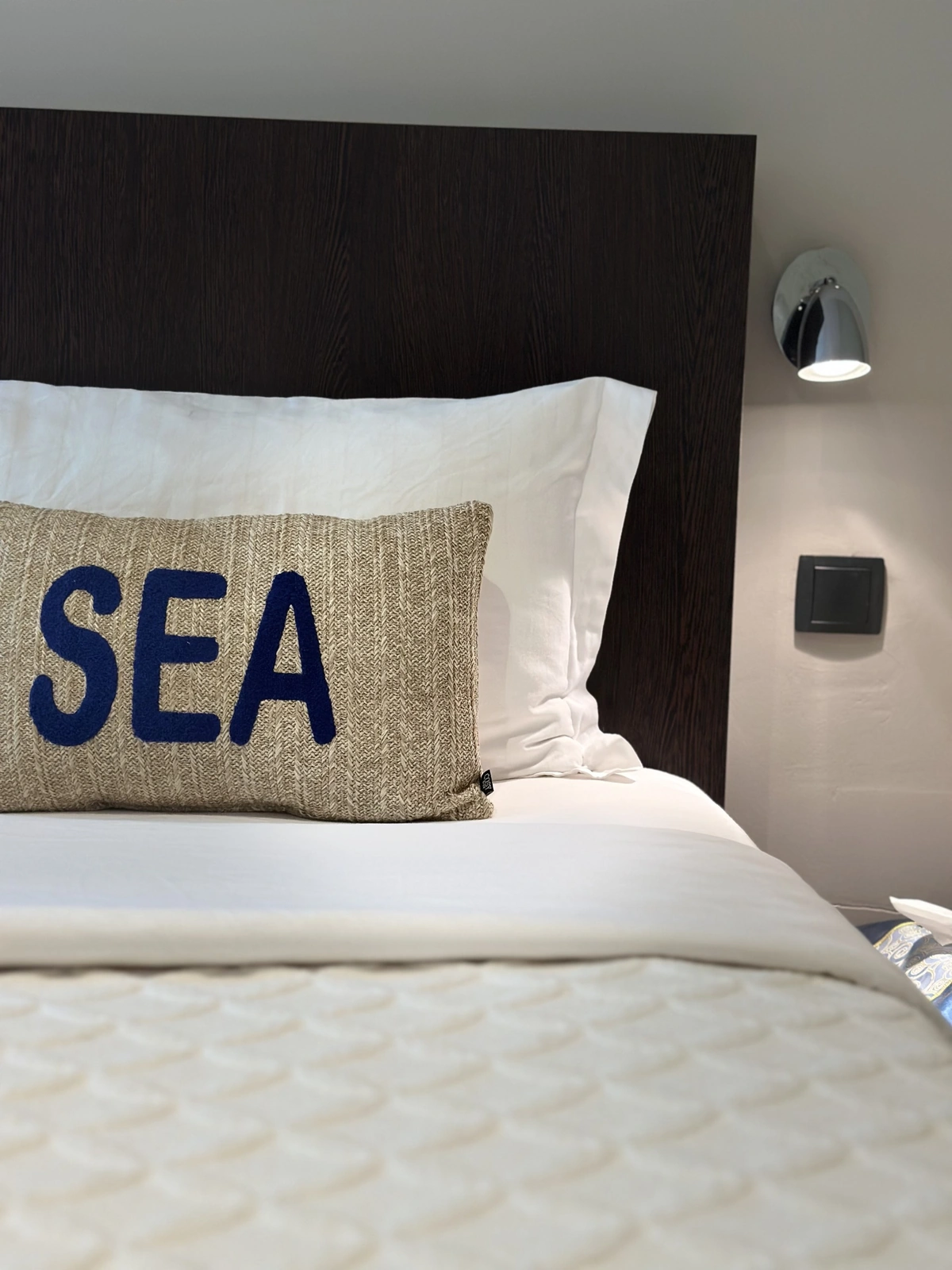 Lit aux draps blancs, coussin brodé « SEA » et tête de lit en bois foncé, hôtel O Mamma Mia à Lourmarin