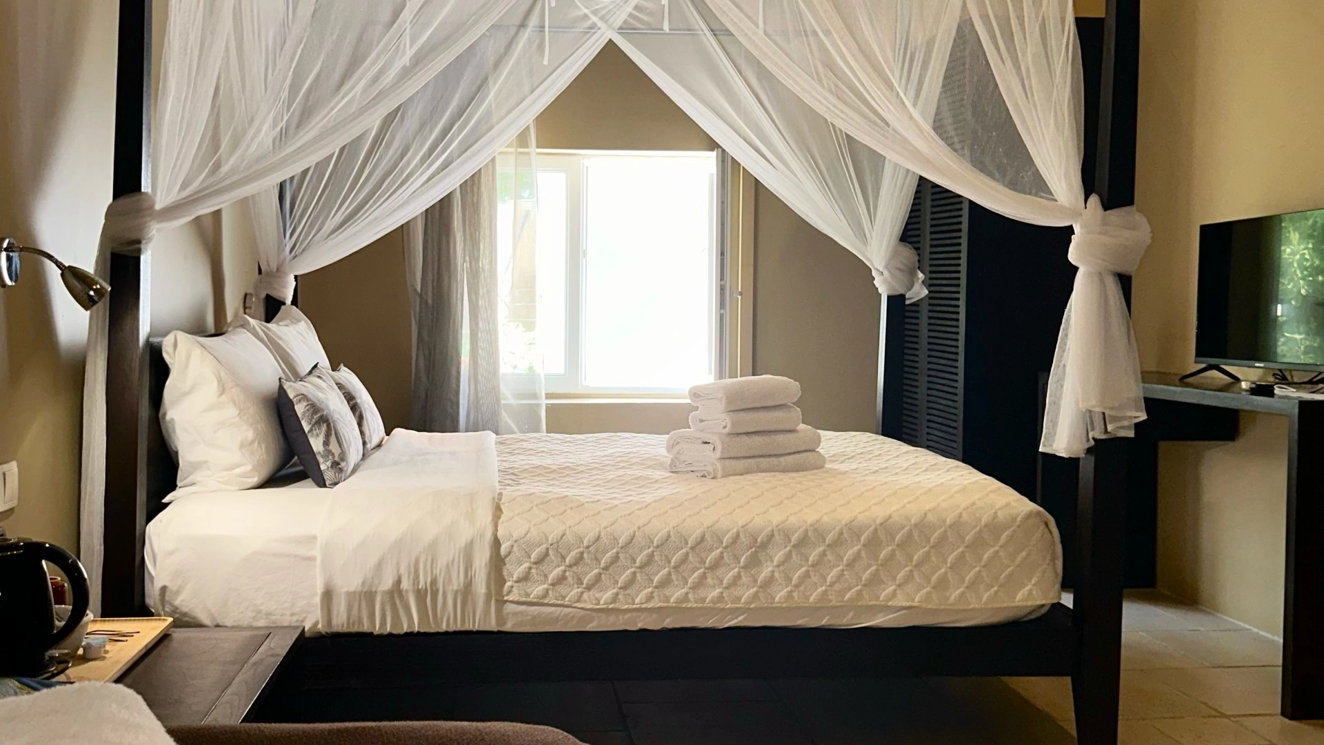 Chambre au lit à baldaquin sous moustiquaire, fenêtre ouverte sur la lumière du jardin, hôtel O Mamma Mia à Lourmarin