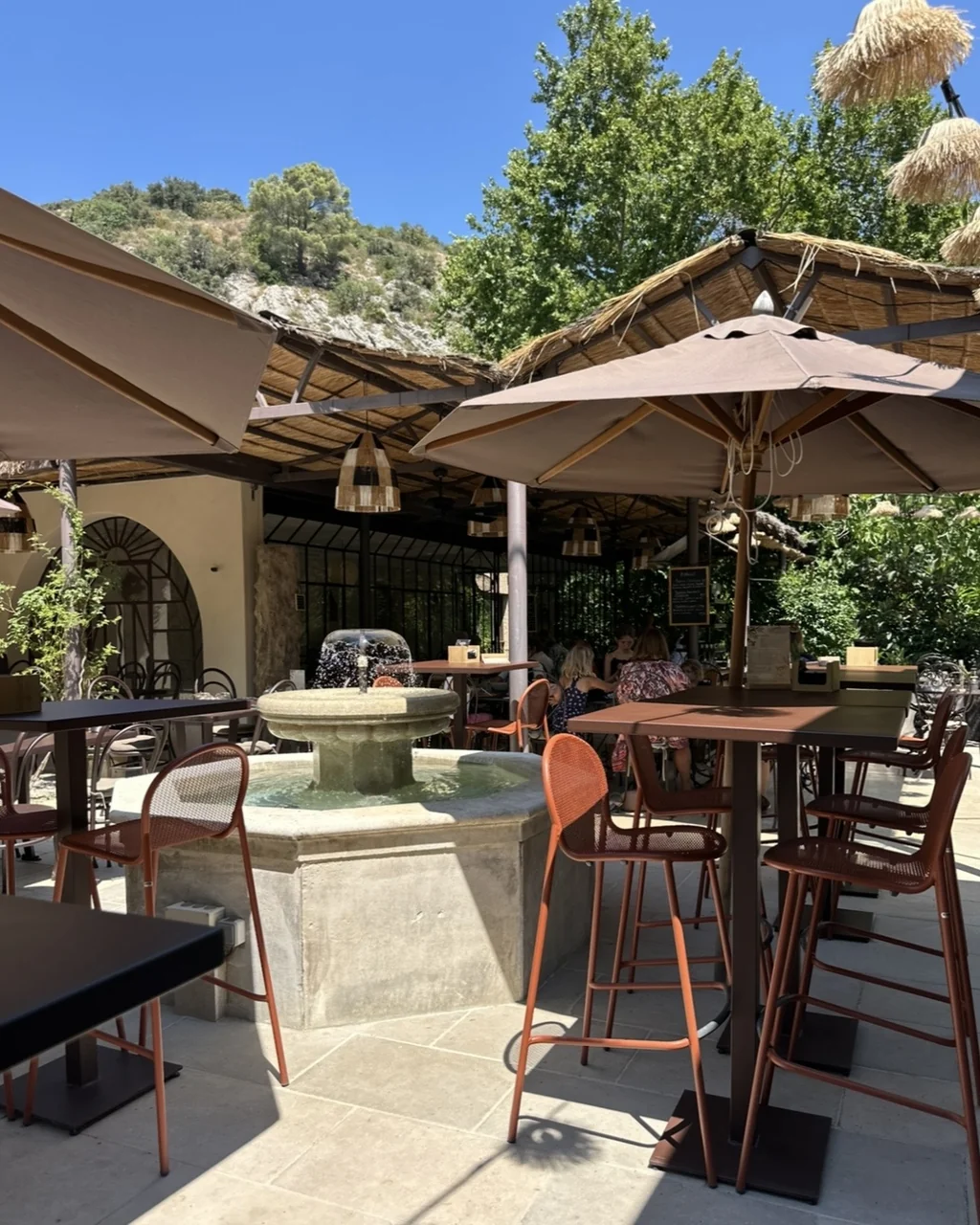 Terrasse, fontaine en pierre et parasols au pied de la falaise, restaurant O Mamma Mia à Lourmarin