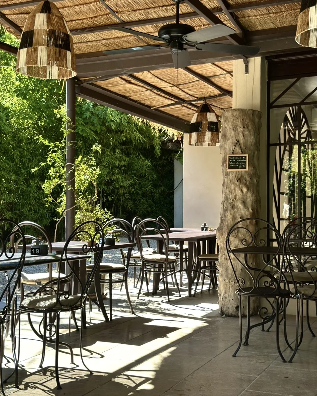 Tables en fer forgé sous les suspensions en rotin et les ventilateurs de la terrasse, restaurant O Mamma Mia à Lourmarin