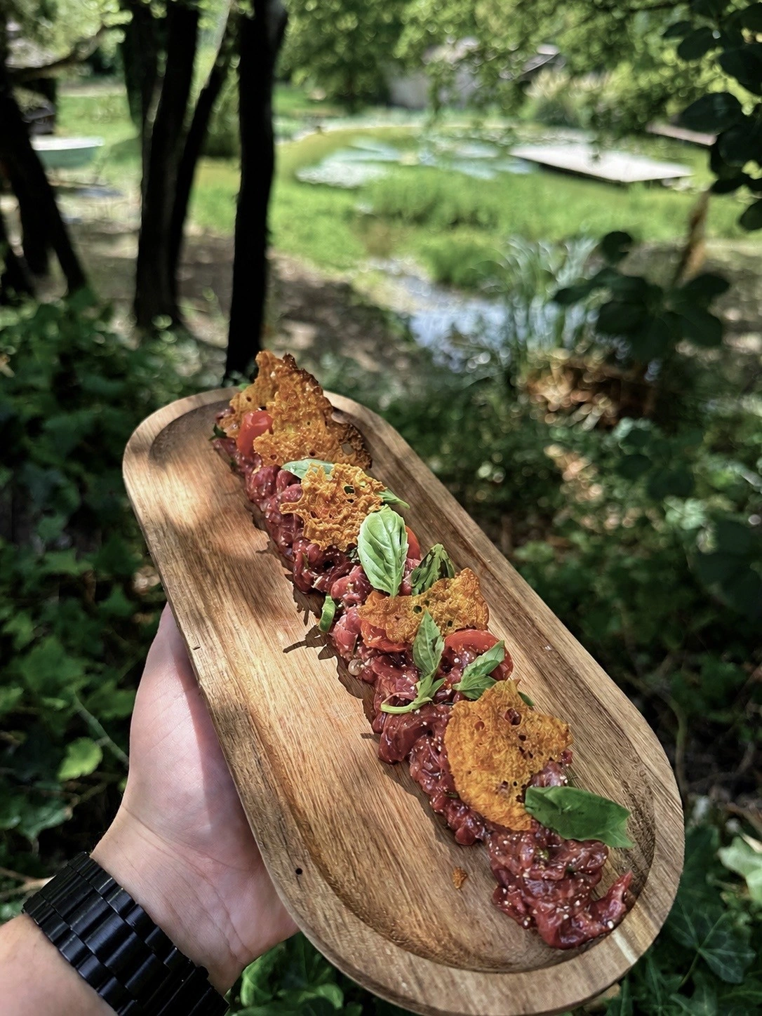 Dolce Tarthaï, tartare de bœuf italo-thaï aux tomates confites et pignons de pin, servi sur une planche en bois devant le bassin naturel, restaurant O Mamma Mia à Lourmarin