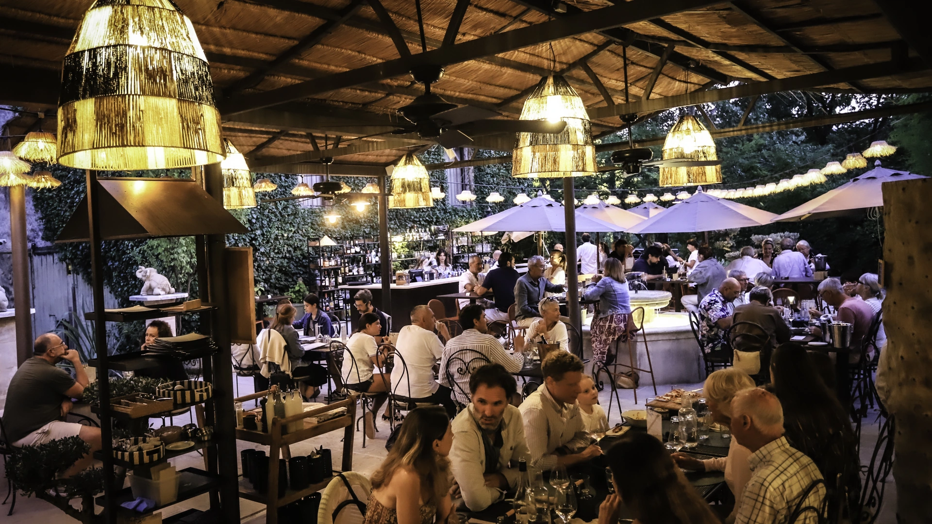 Terrasse du restaurant en soirée, suspensions en rotin allumées et parasols, restaurant O Mamma Mia à Lourmarin