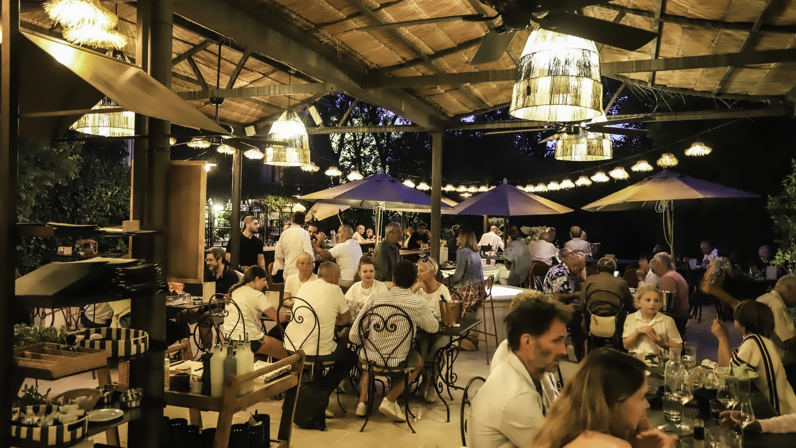 Dîner en terrasse à la nuit tombée, sous les suspensions, les guirlandes et les parasols, restaurant O Mamma Mia à Lourmarin