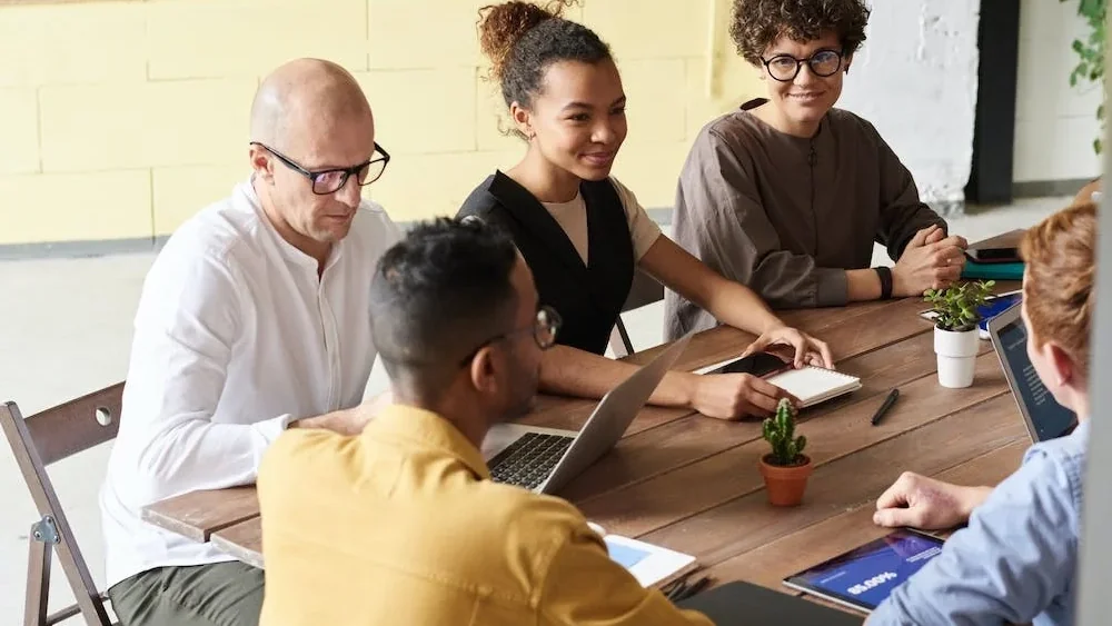 Réunion de travail autour d'une grande table en bois, ordinateurs portables et carnets ouverts