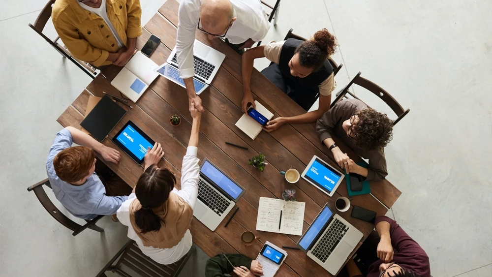 Table de travail vue de dessus : ordinateurs portables, carnets et tasses de café pendant une réunion